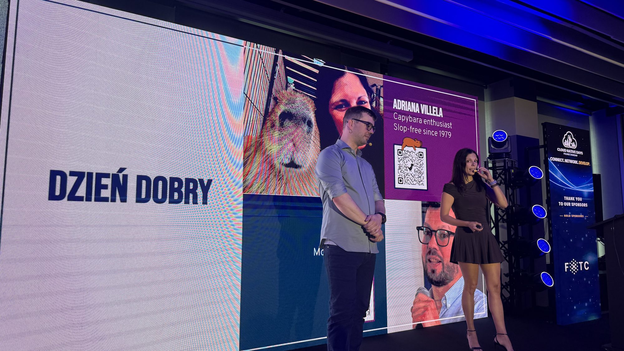 Josh Lee and Adriana Villela on stage next to a Dzień Dobry slide with a capybara and Adriana's bio: Capybara enthusiast, slop-free since 1979