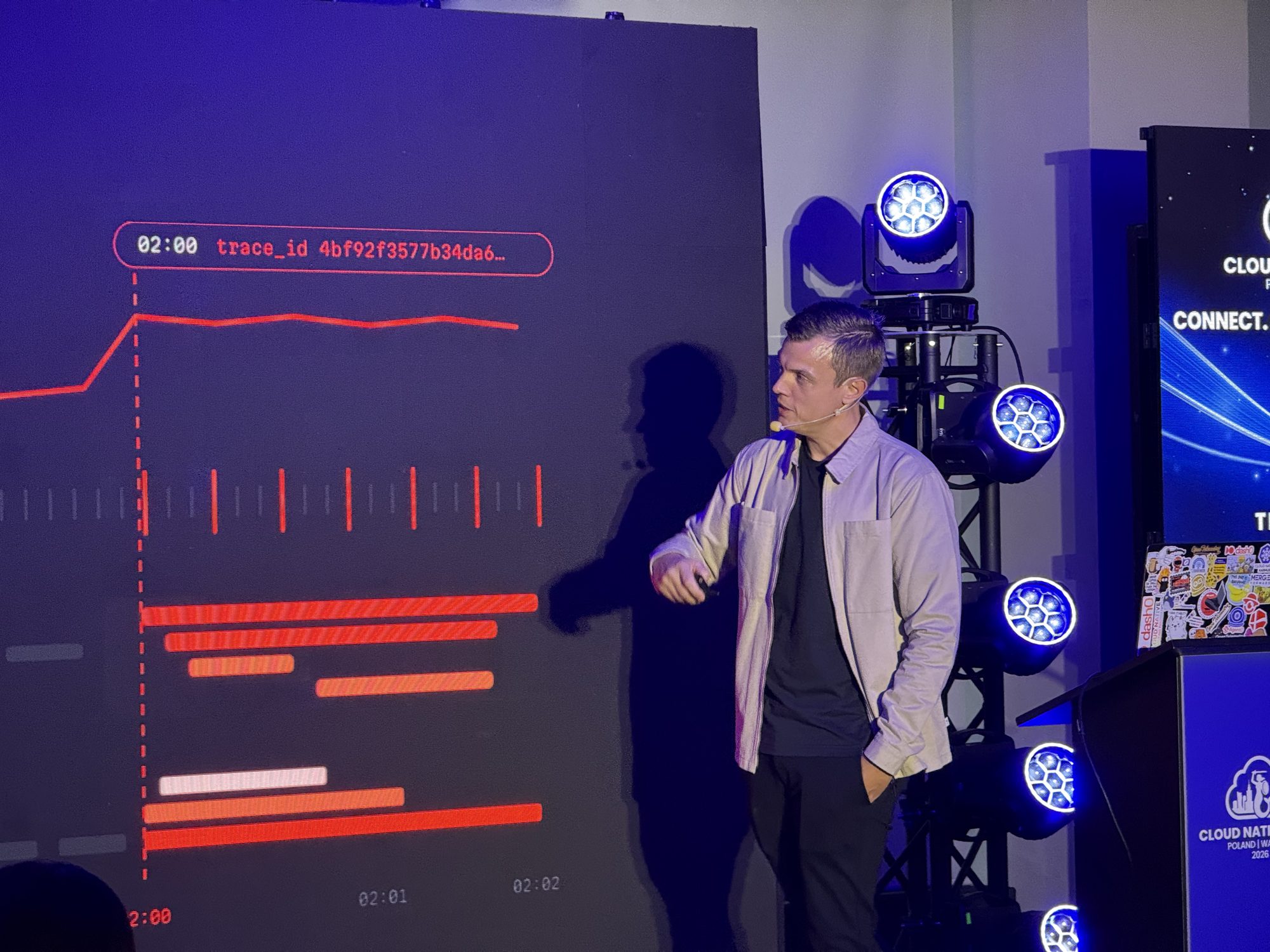 Kasper on stage next to a slide showing a trace waterfall with a trace ID
