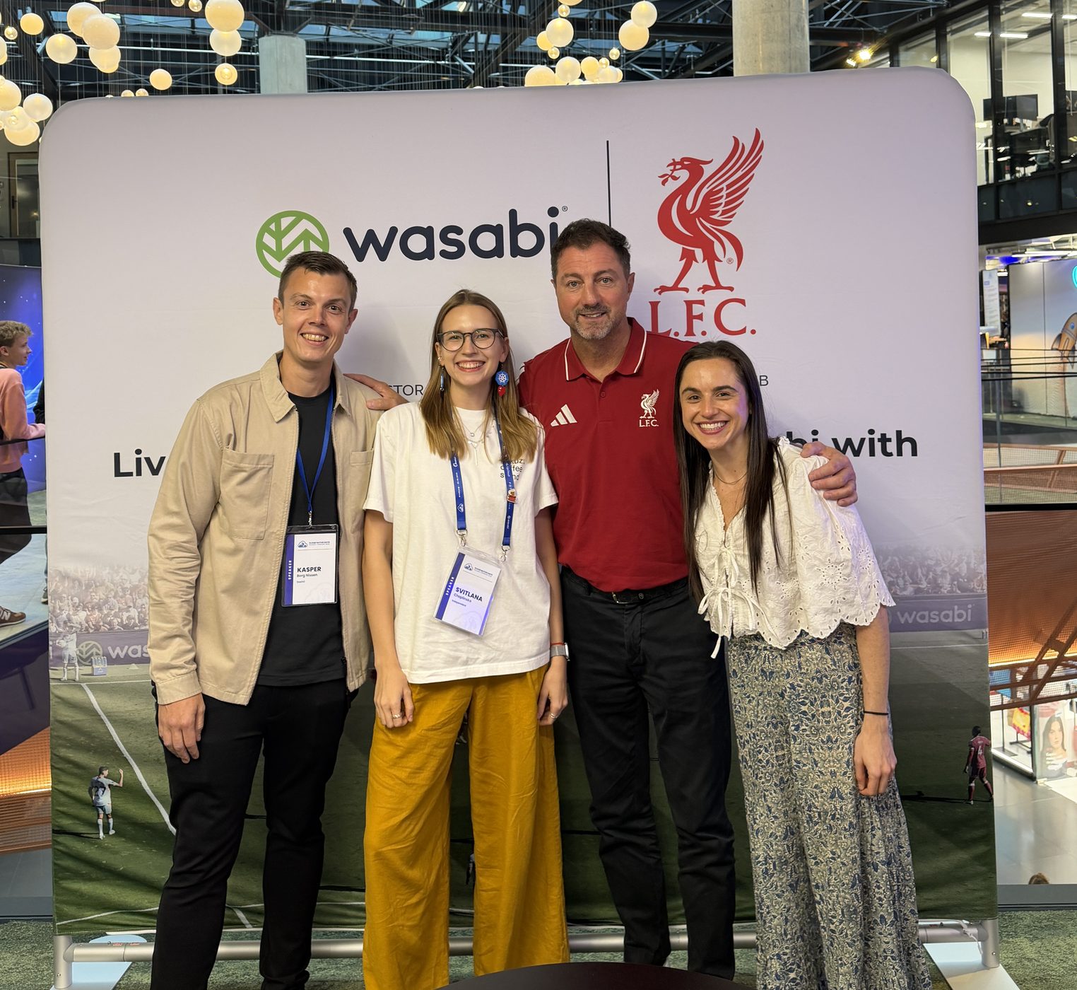 Kasper, Svitlana, Jerzy Dudek in a red Liverpool shirt, and Julia in front of a Wasabi and Liverpool FC backdrop