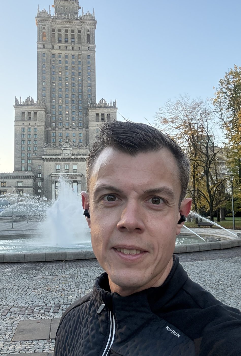 Kasper in a running jacket taking a selfie in front of the Palace of Culture and Science and a fountain