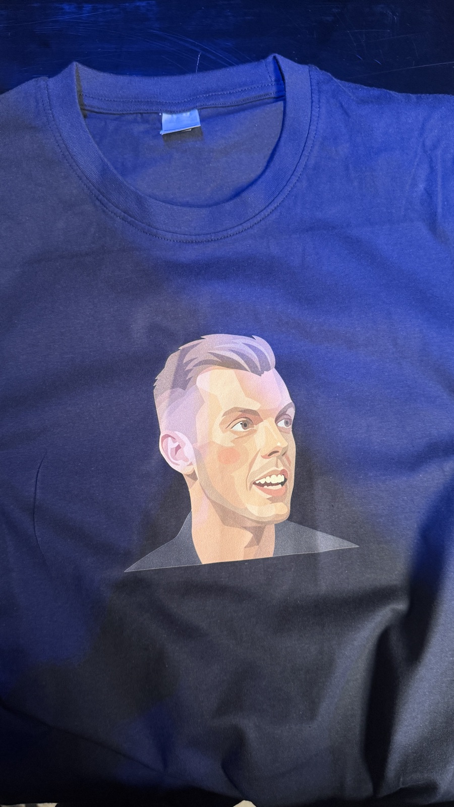 A navy t-shirt printed with an illustrated portrait of Kasper