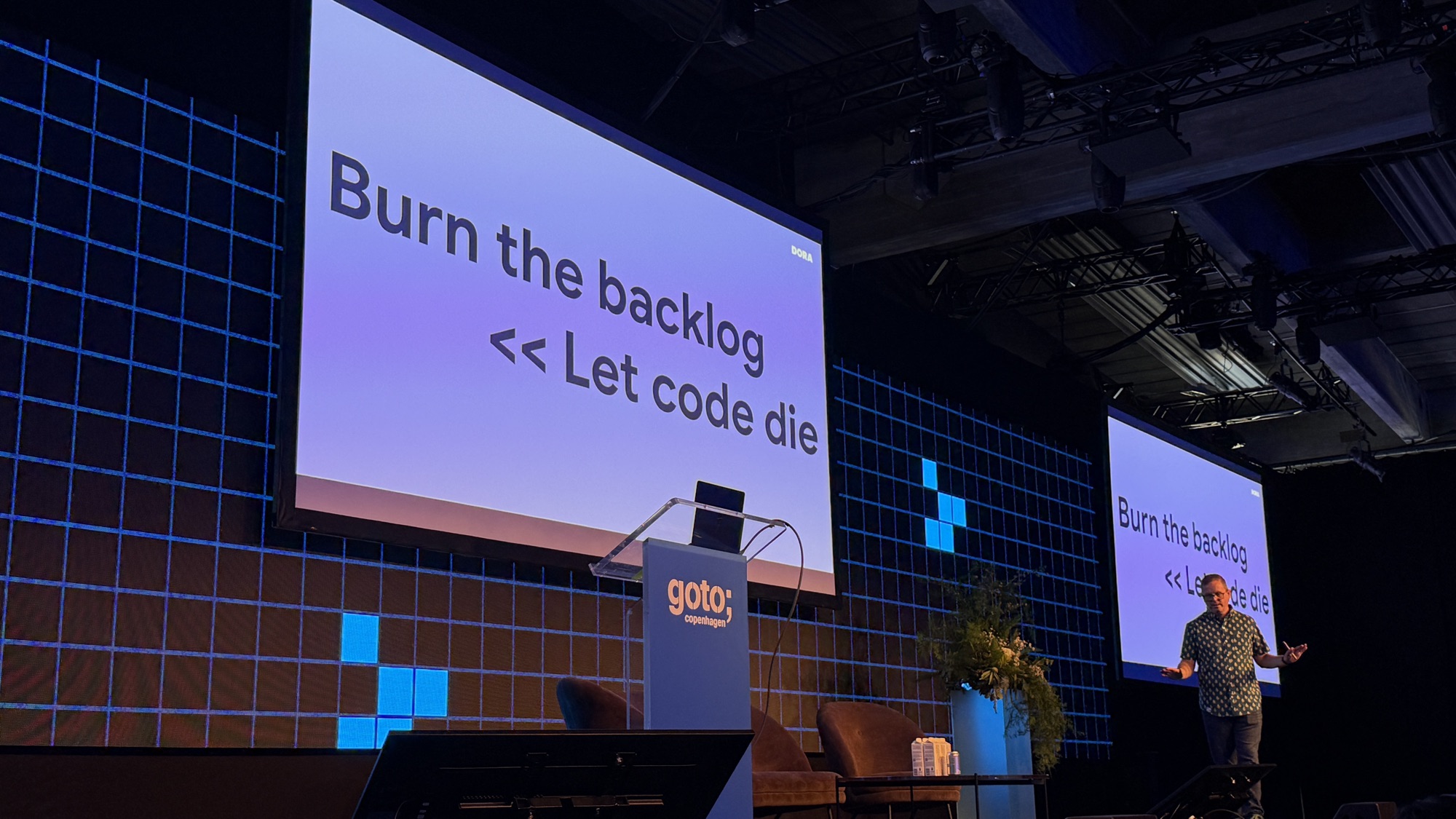 Nathen Harvey on stage under a slide reading Burn the backlog, shift left from Let code die