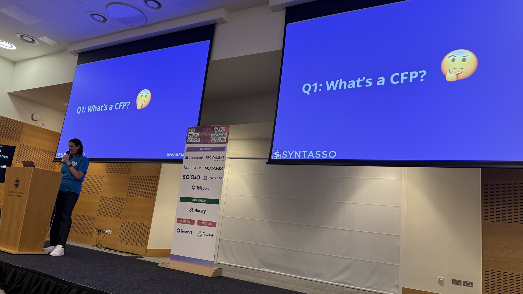 Paula Kennedy on stage between two screens showing Q1: What's a CFP?