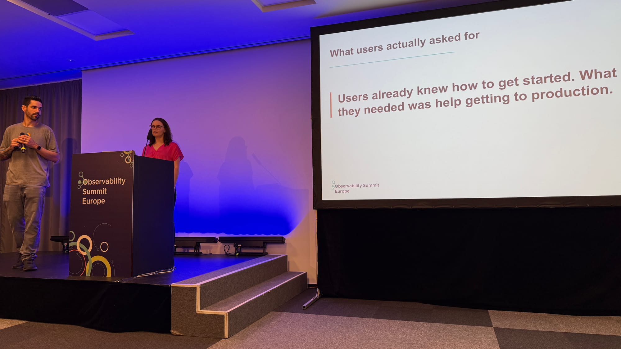 Juliano and Johanna on stage next to a slide reading: Users already knew how to get started. What they needed was help getting to production.