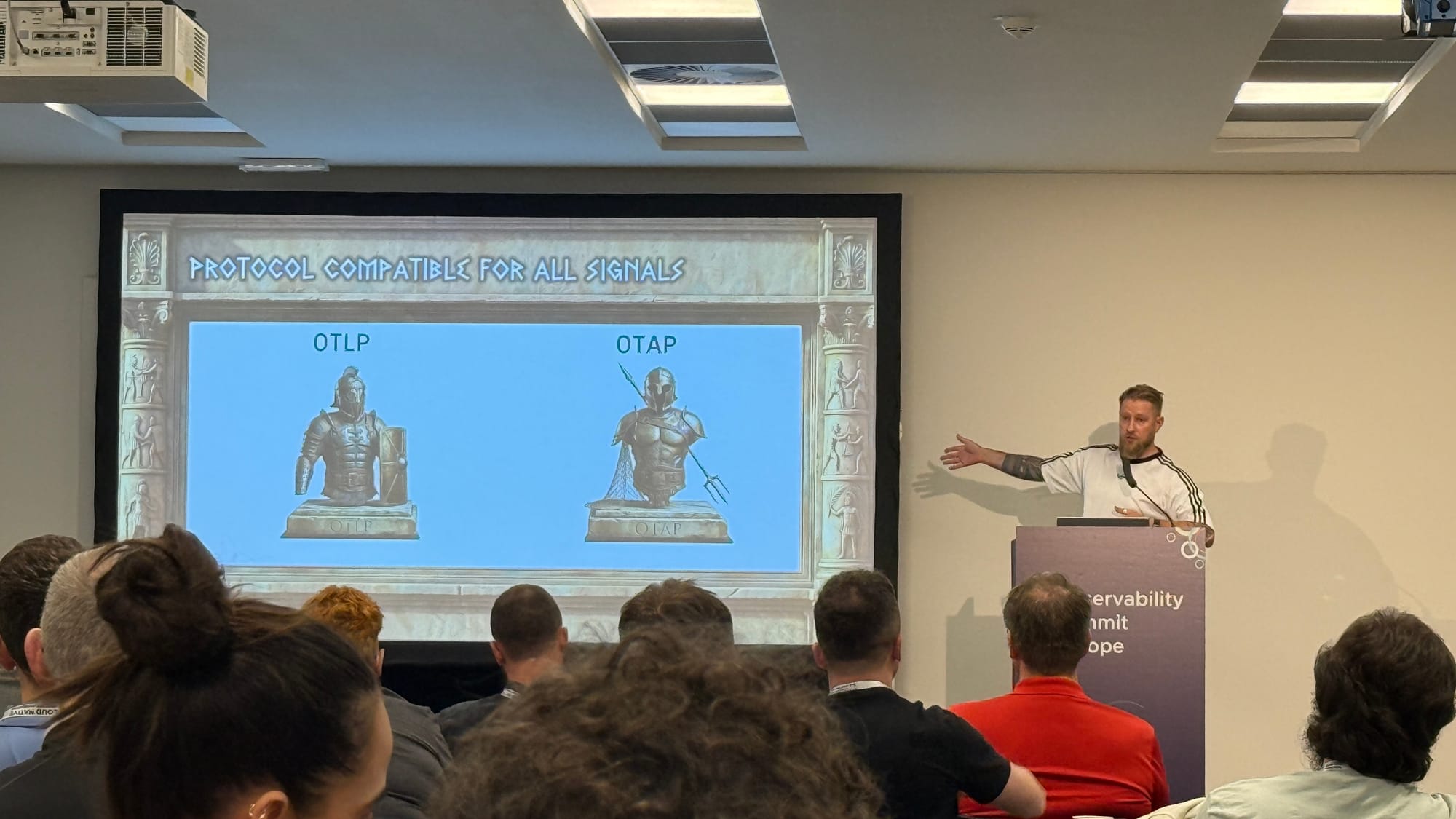 Henrik Rexed in front of a slide titled Protocol compatible for all signals, showing two gladiator busts labelled OTLP and OTAP