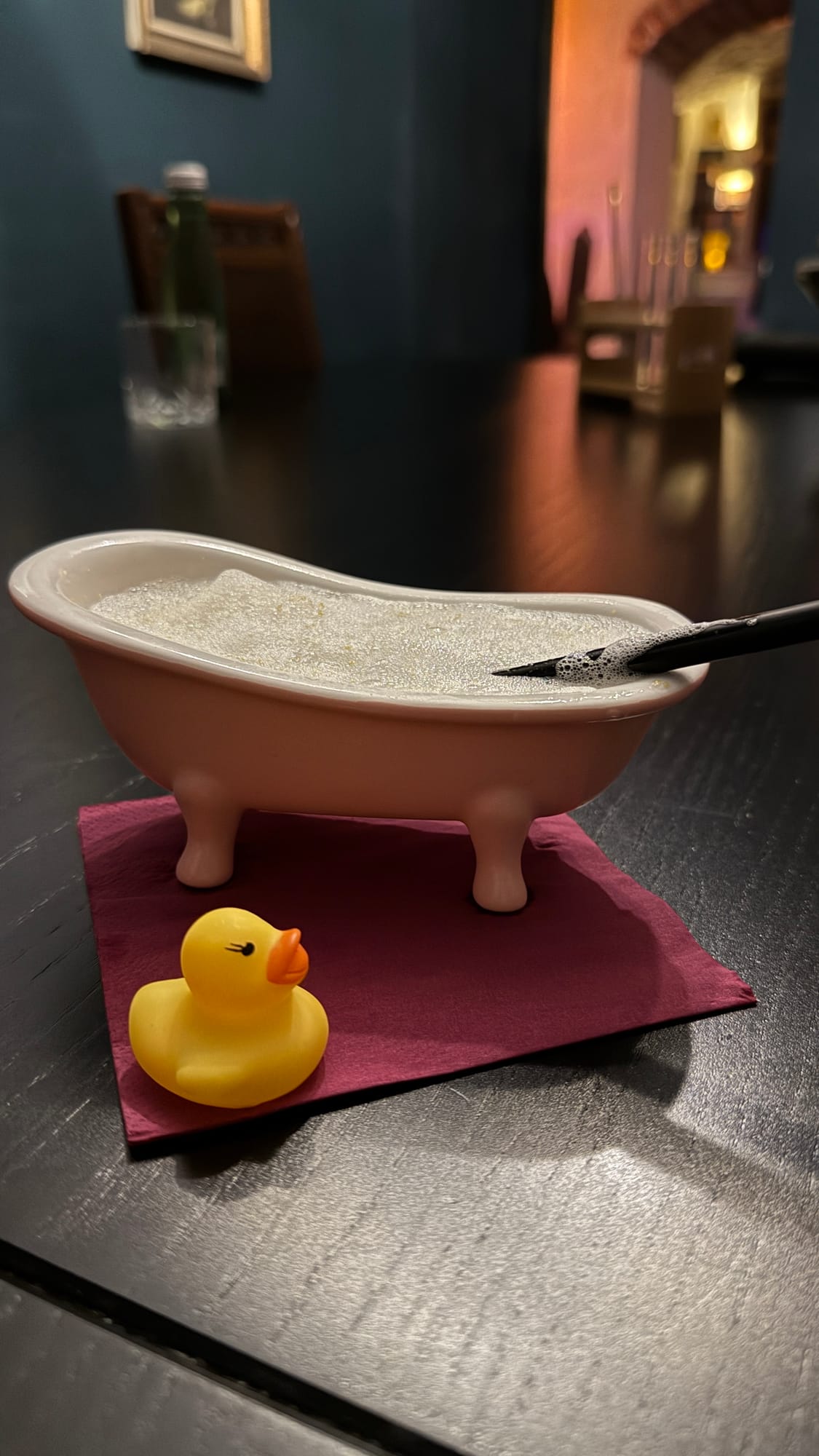 A cocktail served in a small pink bathtub with a rubber duck next to it