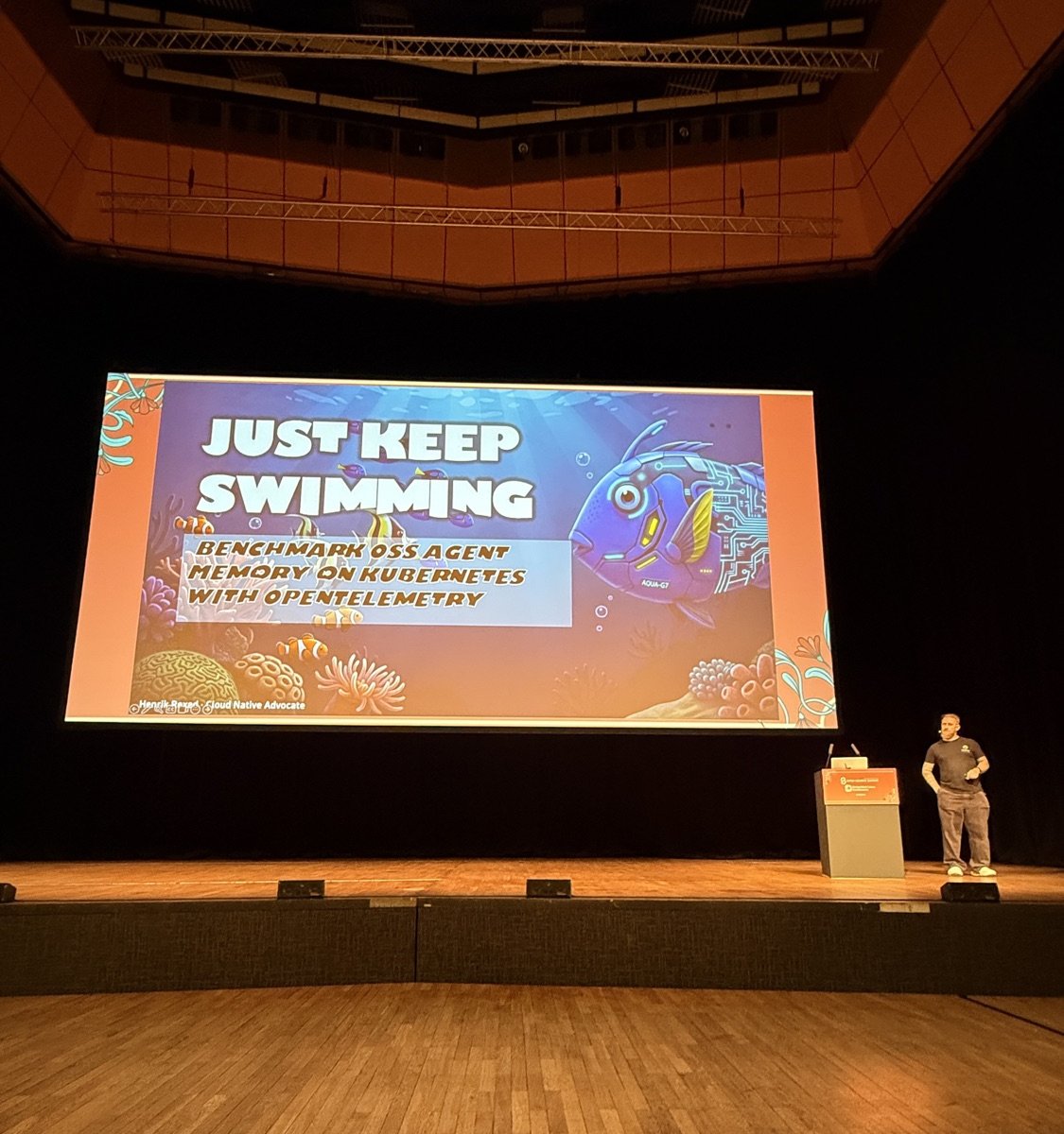Henrik Rexed on the wooden stage in Forum Hall next to the title slide Just Keep Swimming, with a robotic blue tang fish