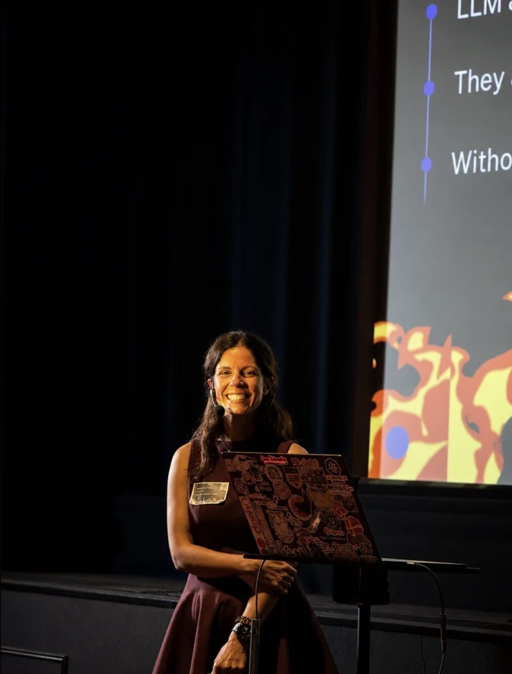 Adriana smiling mid-talk next to the projected slide